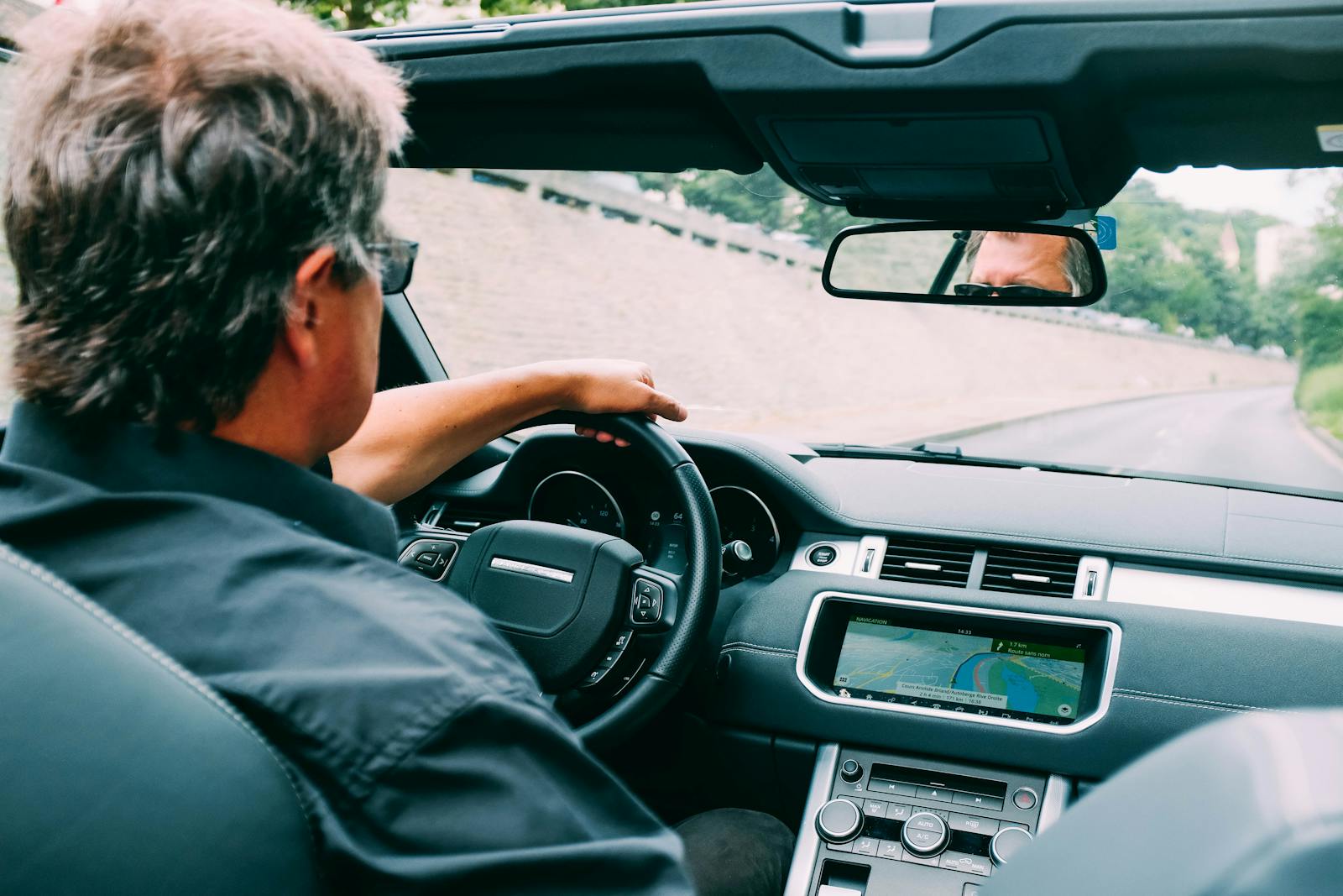 A man driving a convertible auto on a scenic highway with a focus on the dashboard.